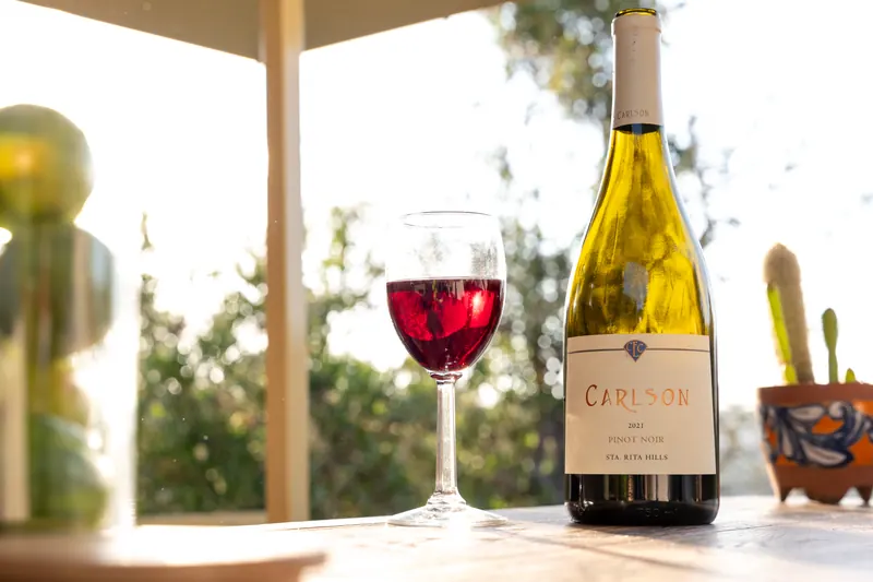 A glass of red wine and a bottle of Chardonnay on the bar top
