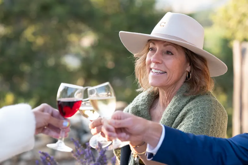 A guest in a wide-brimmed hat smiling as glasses meet