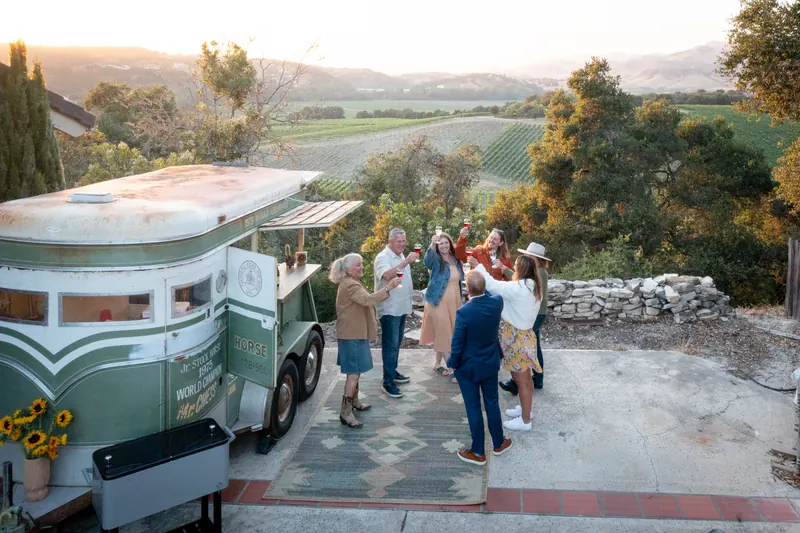 Guests gathered around the trailer at golden hour above the vineyards
