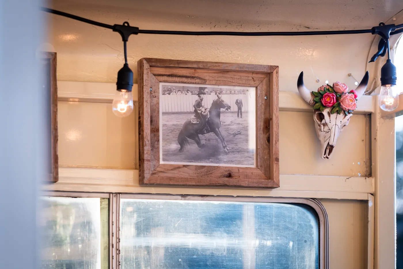 A framed black-and-white photo of a reined cow horse competitor hangs inside the trailer, beside a floral steer skull and string lights