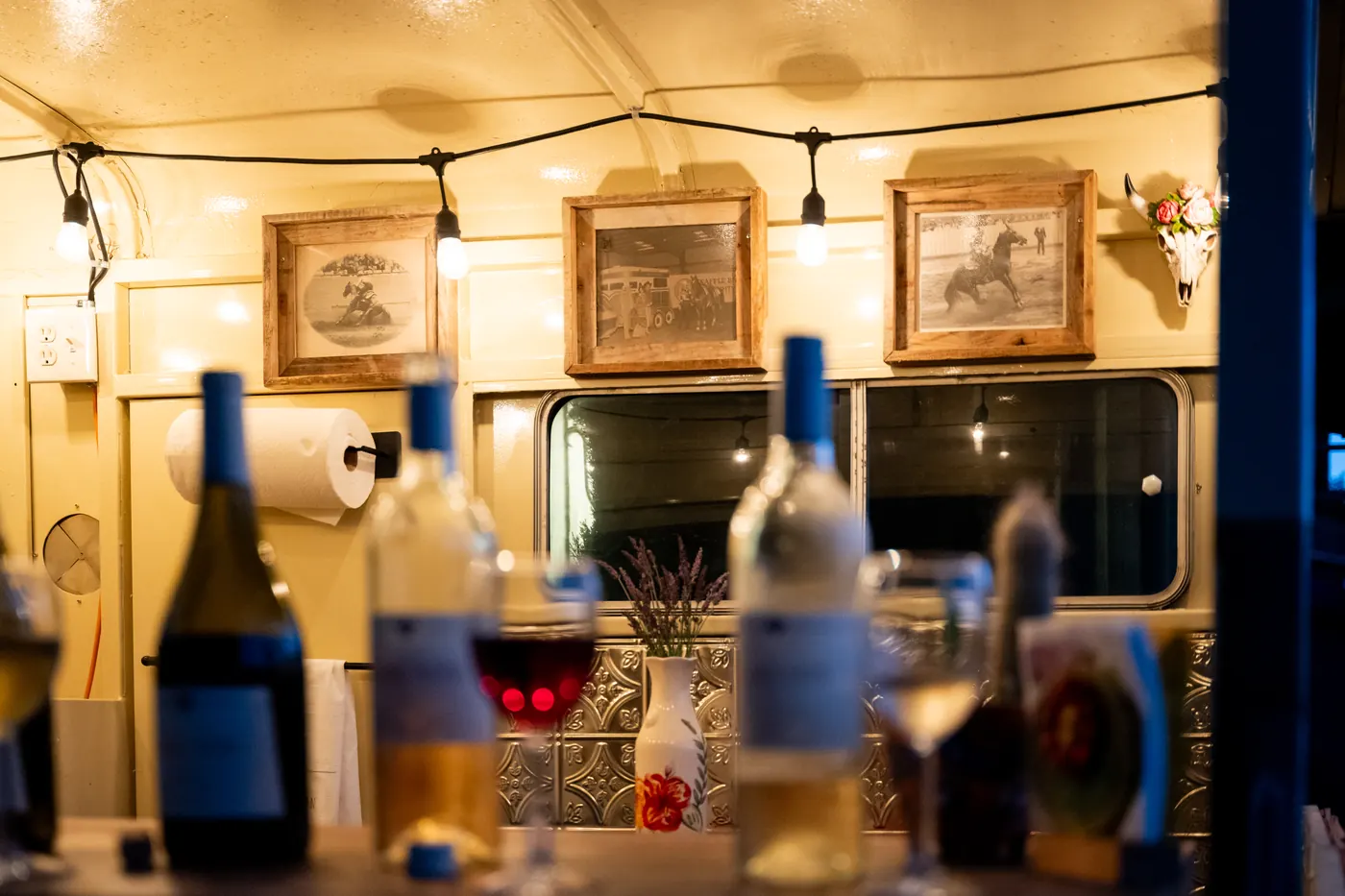 Inside the trailer at night: wine bottles, string lights and framed horse show photographs