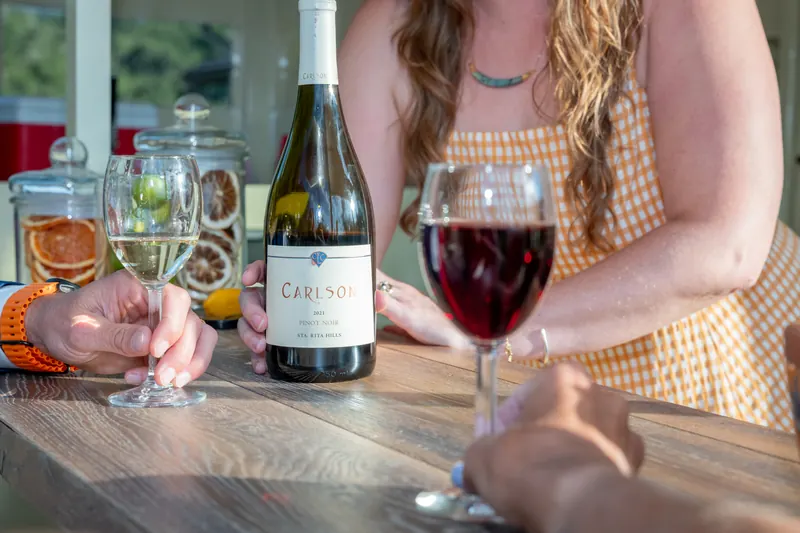 A bottle of white wine and glasses of red and white on the wooden bar top